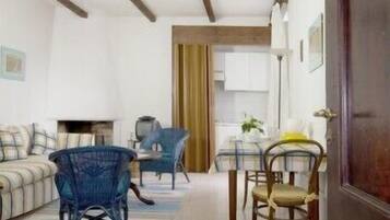 Ein Wohnzimmer mit einer Couch, zwei blauen Sesseln, einem Holzesstisch mit Stühlen und einer Küche im Hintergrund.