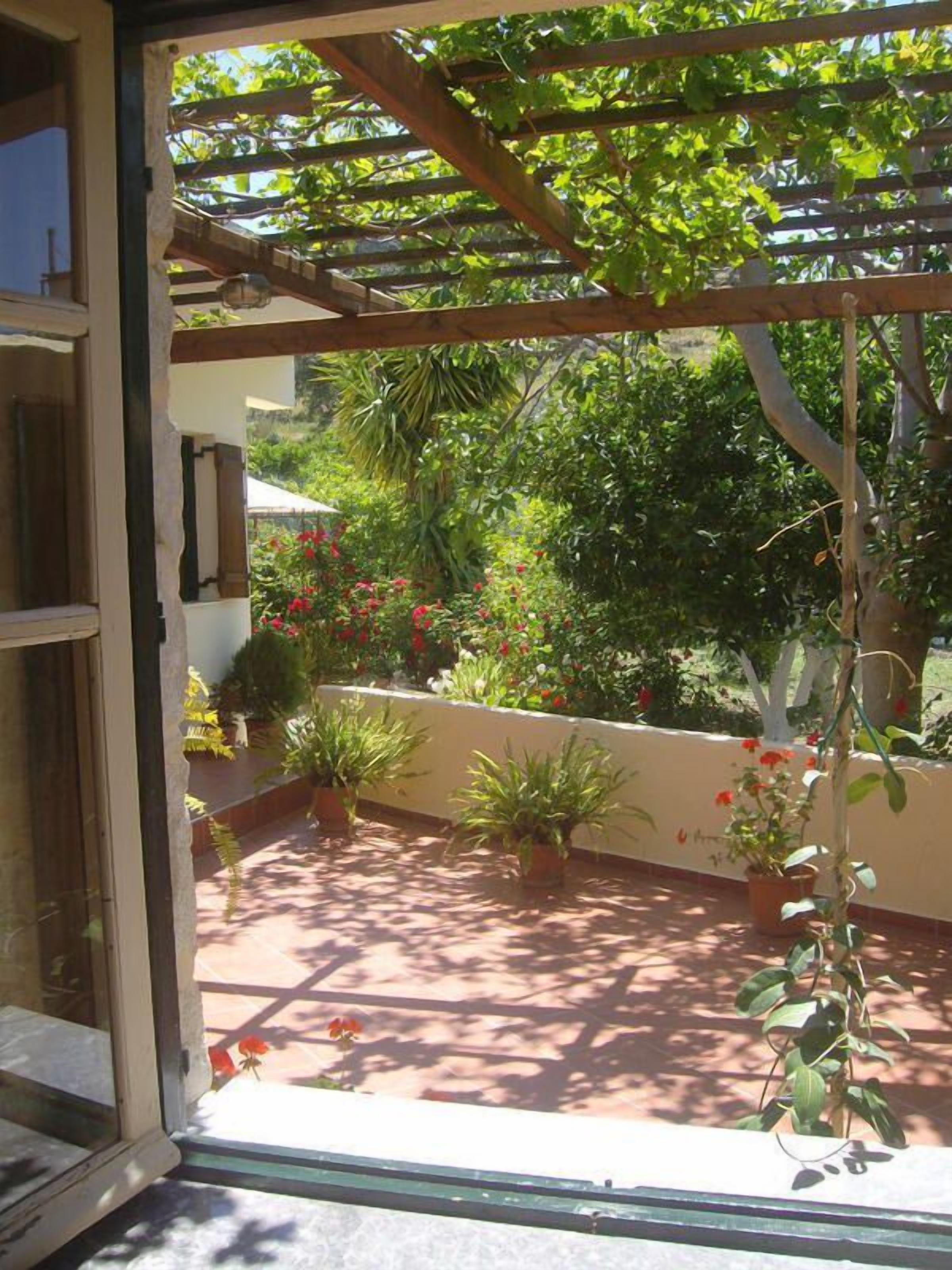 An open door leading to a garden with potted plants and a pergola structure.