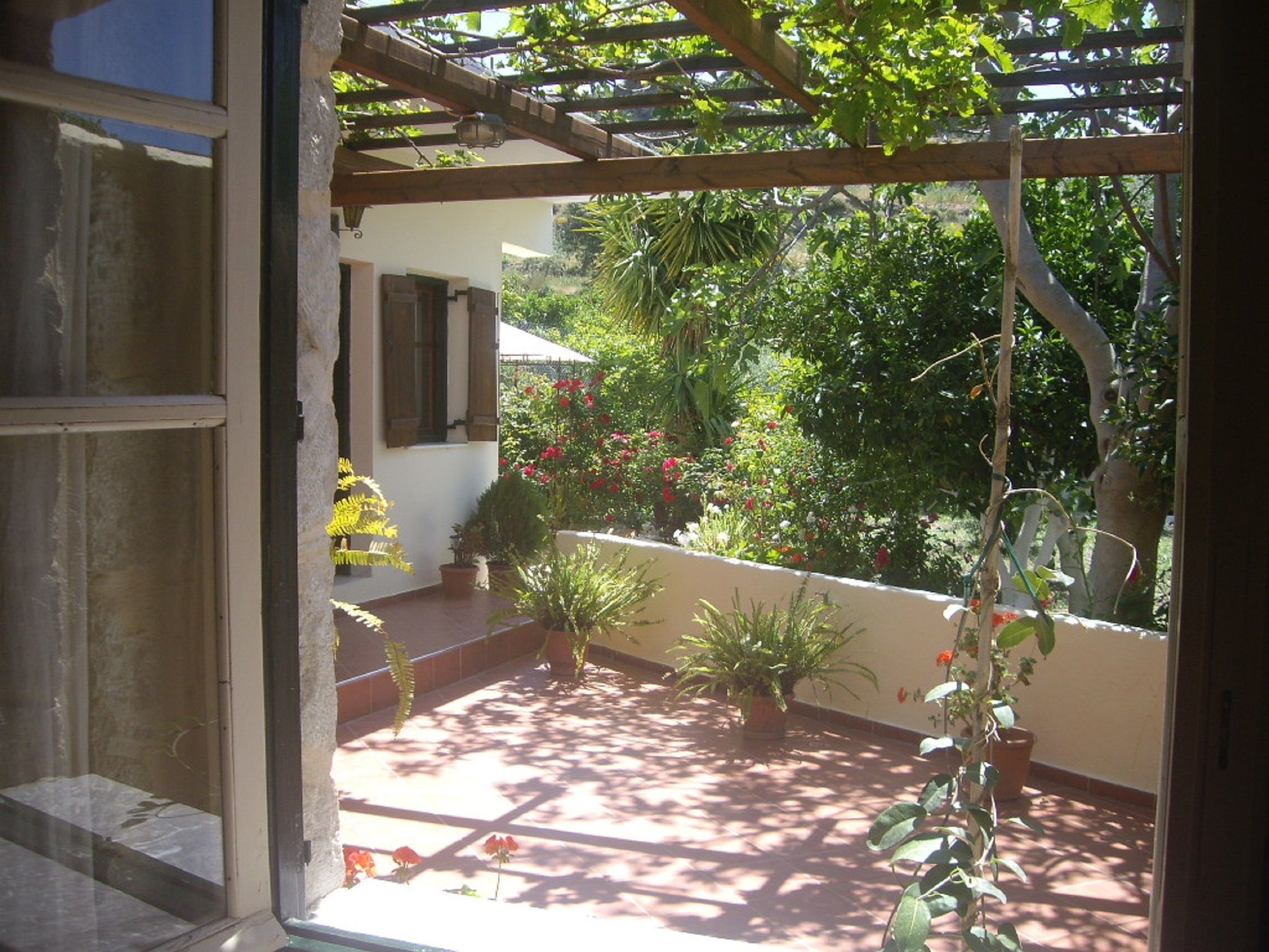 A covered patio with potted plants and a view of a garden.