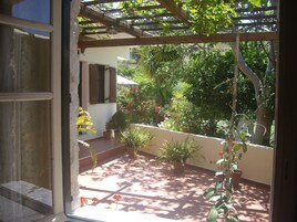 Une terrasse couverte, agrémentée de plantes en pot et offrant une vue sur un jardin.