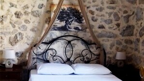 Un lit à baldaquin, un mur en pierre et deux tables de chevet avec des lampes.