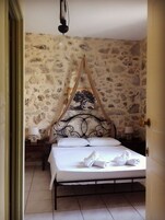 Una cama con dosel, una pared de piedra y una mesita de noche con lámpara.
