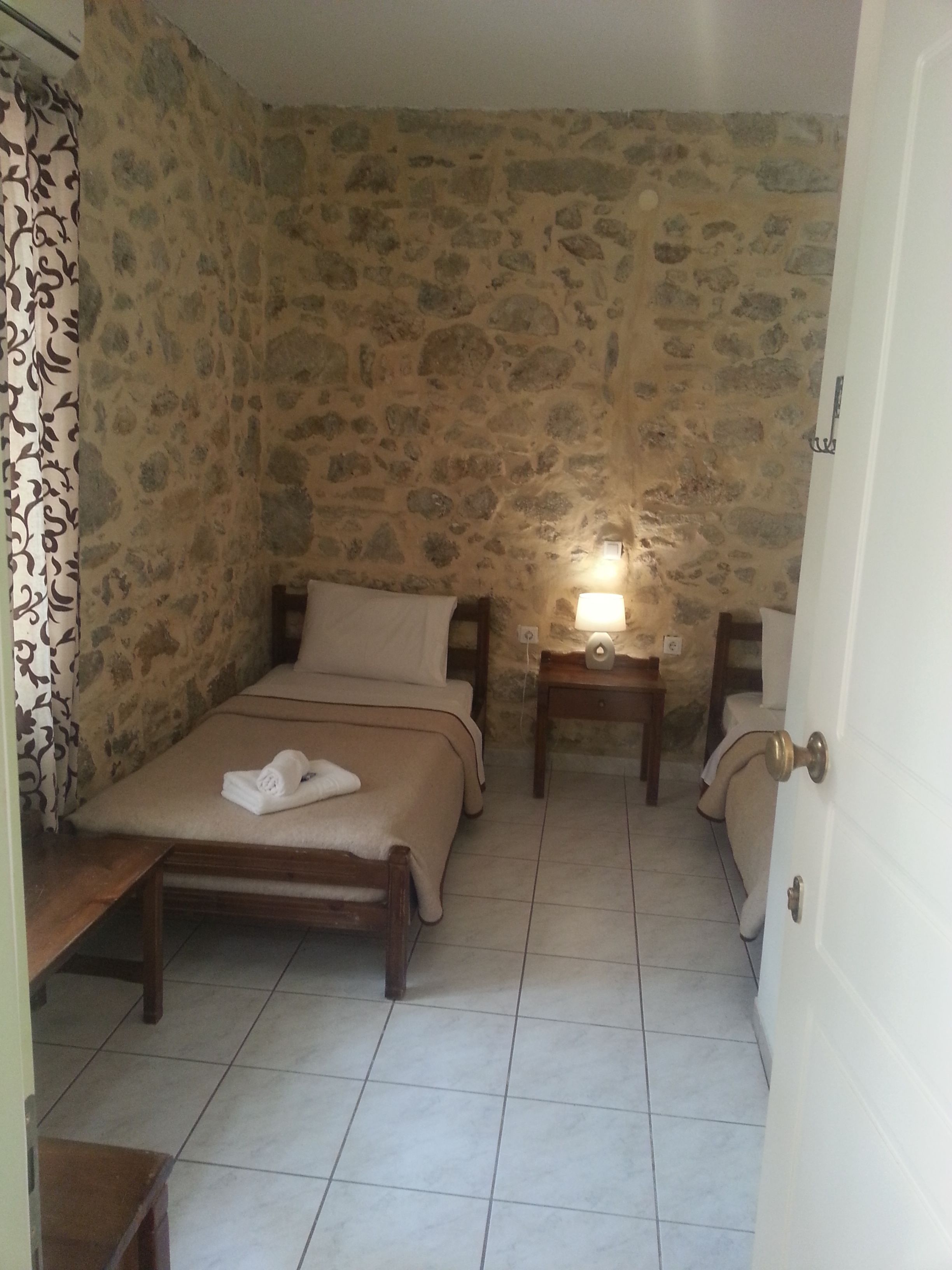 Un dormitorio con pared de piedra, una cama con cabecero de madera, una mesita de noche con lámpara y una puerta.