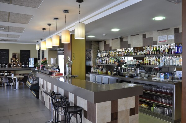 Una zona de bar con barra, estantes llenos de botellas y asientos.