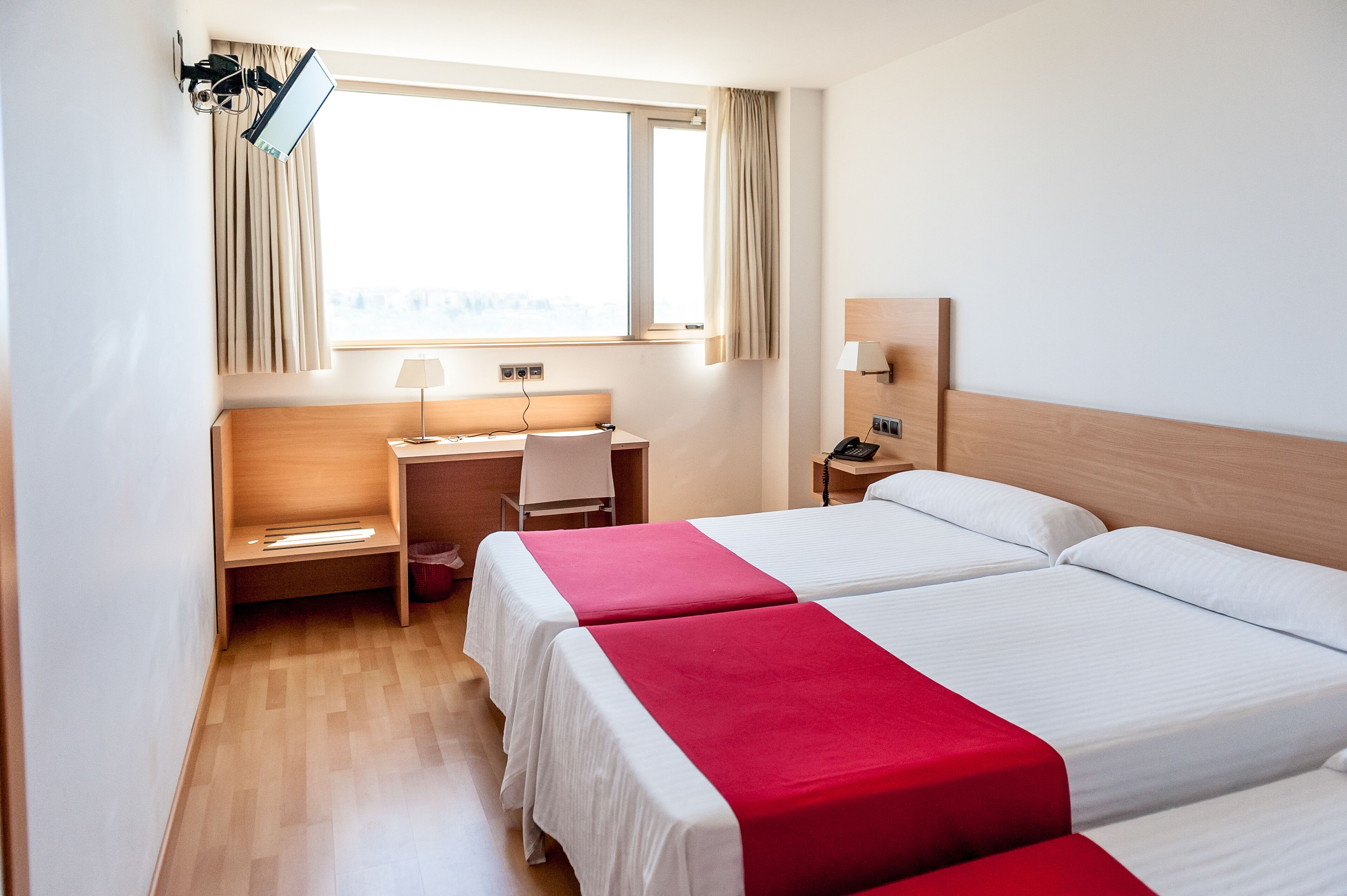 A hotel room with two beds, a desk, a chair, a lamp, and a window with curtains.