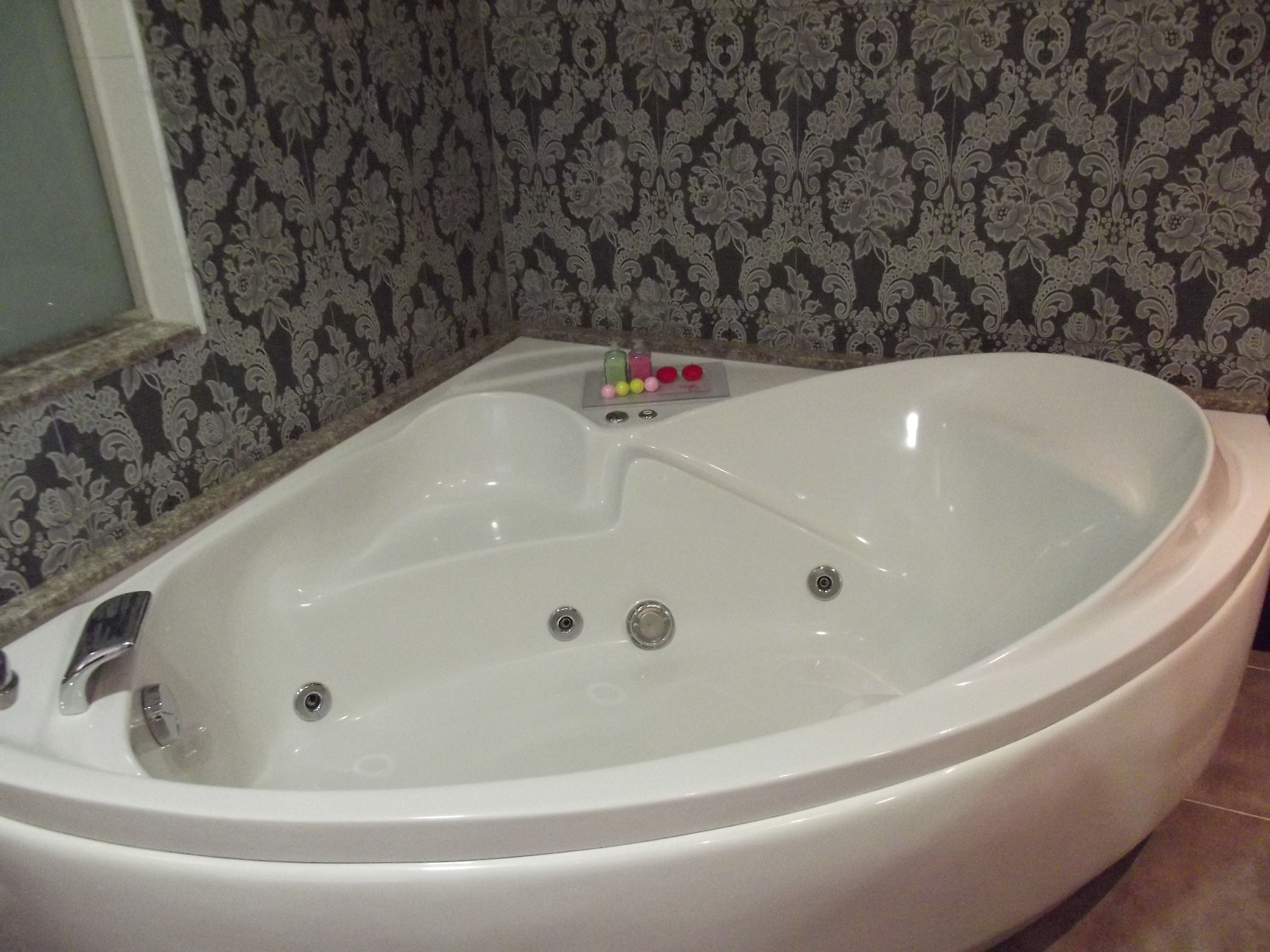 Una bañera blanca grande y separada, con varios grifos y un panel de control con botones de colores.