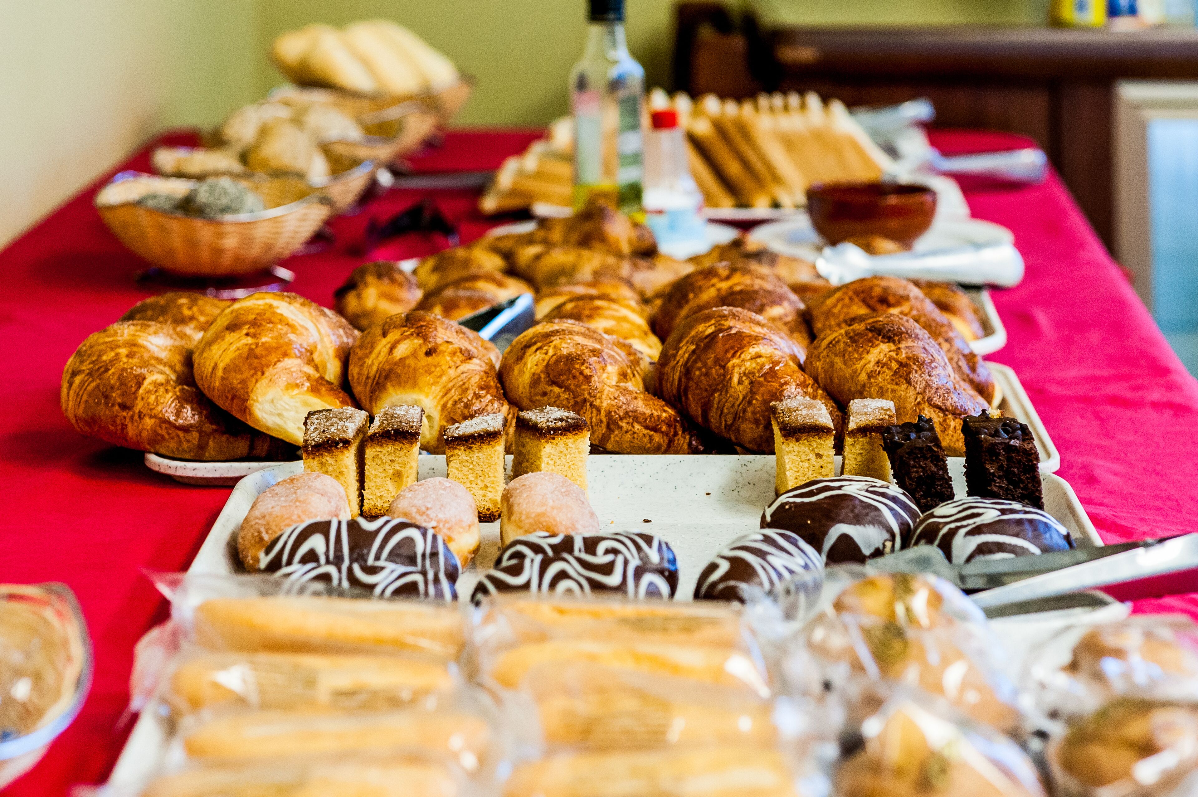 Une table garnie d’un assortiment de viennoiseries et de pâtisseries, notamment des croissants et des produits enrobés de chocolat.
