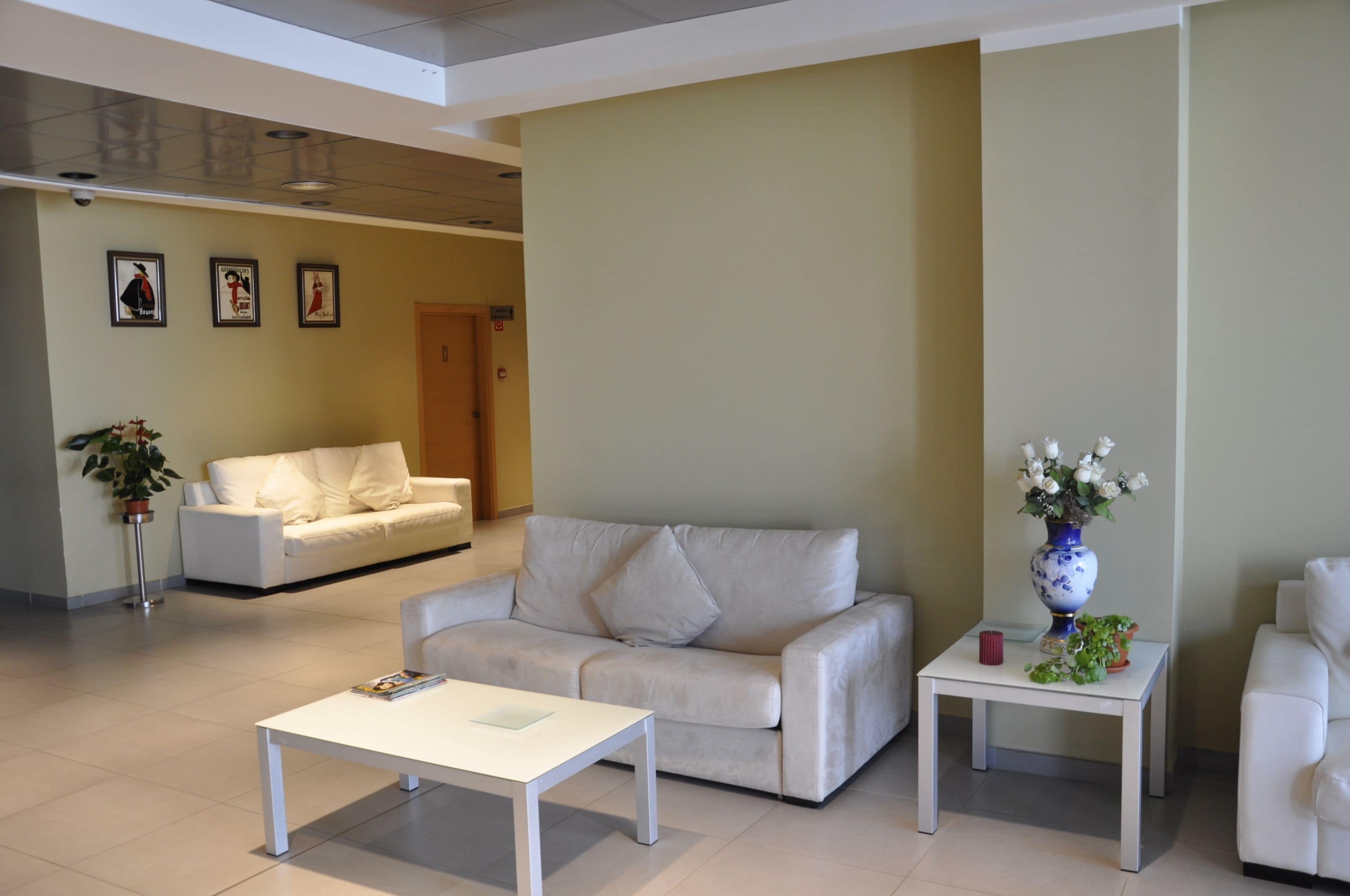 A modern living room with a white sofa, a white coffee table, and a small side table with a vase of flowers.