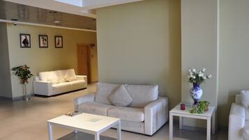 A modern living room with a white sofa, a white coffee table, and a small side table with a vase of flowers.