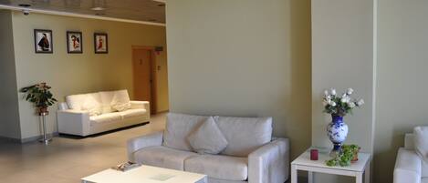 A modern living room with a white sofa, a white coffee table, and a small side table with a vase of flowers.