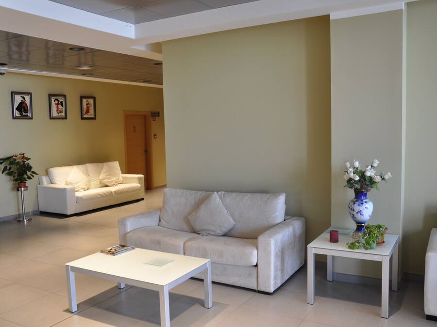 A modern living room with a white sofa, a white coffee table, and a small side table with a vase of flowers.