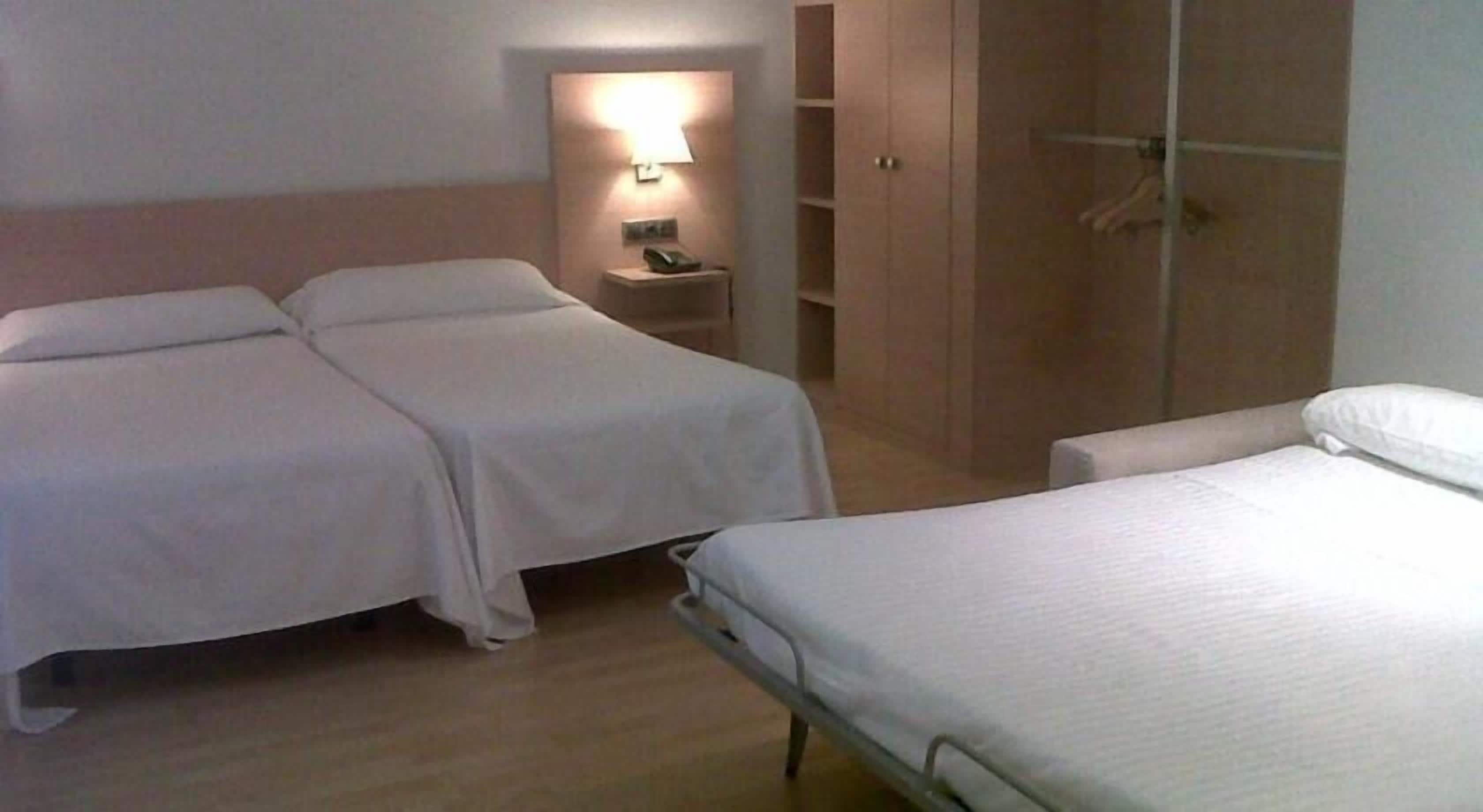 Habitación de hotel con dos camas, una mesita de noche con lámpara y un armario.