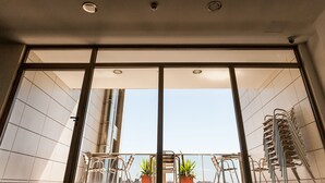 Uitzicht vanuit een kamer met grote ramen, een plafond met inbouwverlichting en een balkon met stoelen en plantenpotten.
