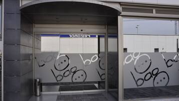 En modern entré till en byggnad med en glasdörr, en metallbehållare för sopor och en blå skylt ovanför dörren.