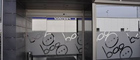 A modern building entrance with a glass door, a metal trash bin, and a blue sign above the door.