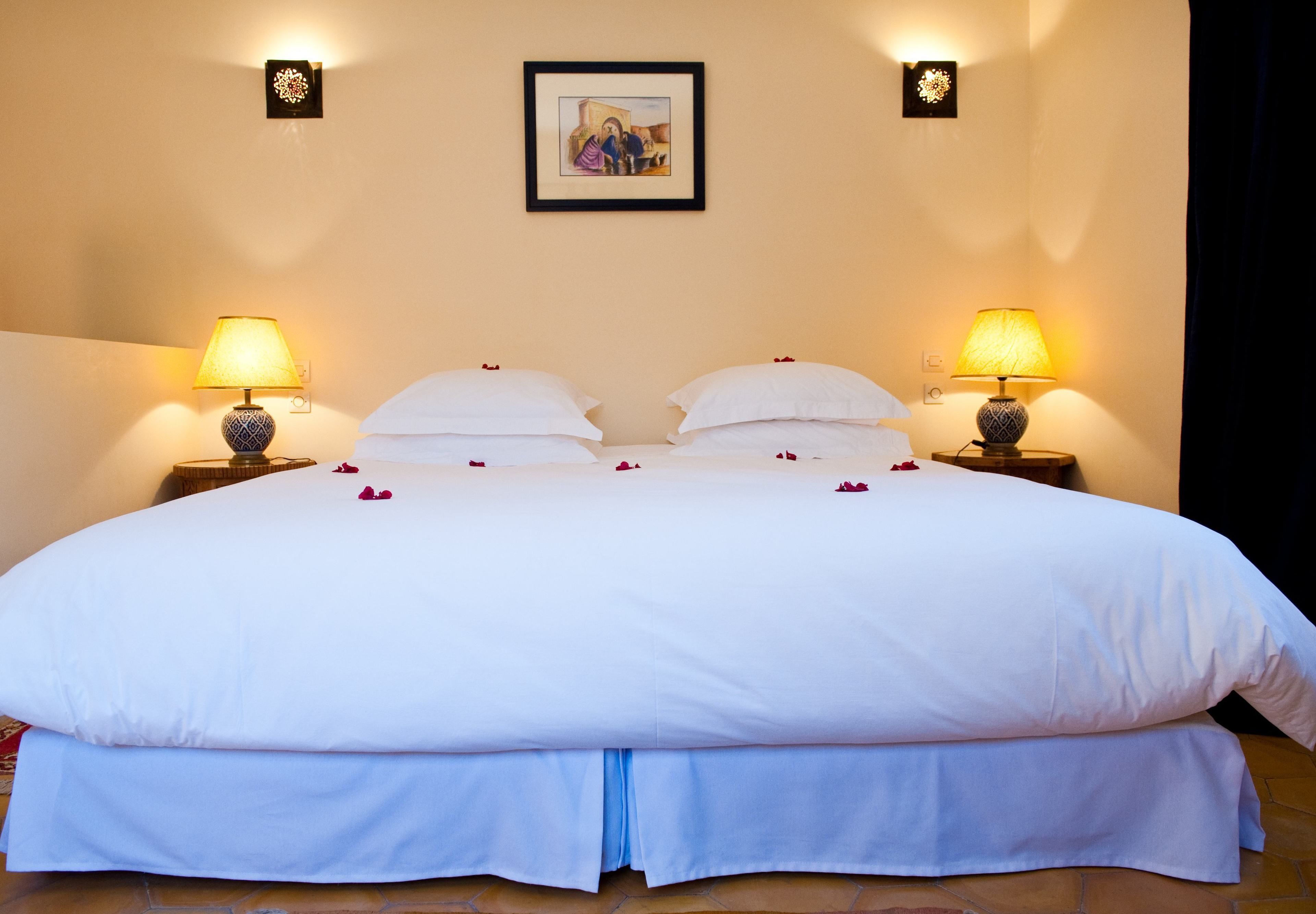 A large bed with white linens, two bedside lamps, and a framed picture on the wall.