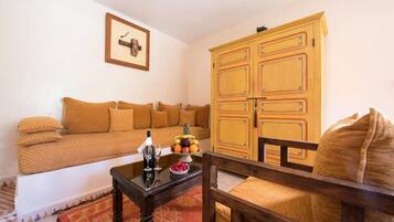 Sala de estar com sofá, armário de madeira e uma mesa pequena com uma fruteira e uma garrafa.