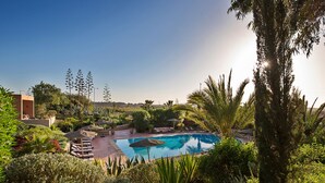 A swimming pool surrounded by lush greenery and palm trees, with a clear sky above. - Dar Maktoub (Inezgane)