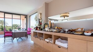A modern dining area with a buffet setup, including a variety of food items and beverages, a dining table with chairs, and a view of the outdoors. - Dar Maktoub (Inezgane)