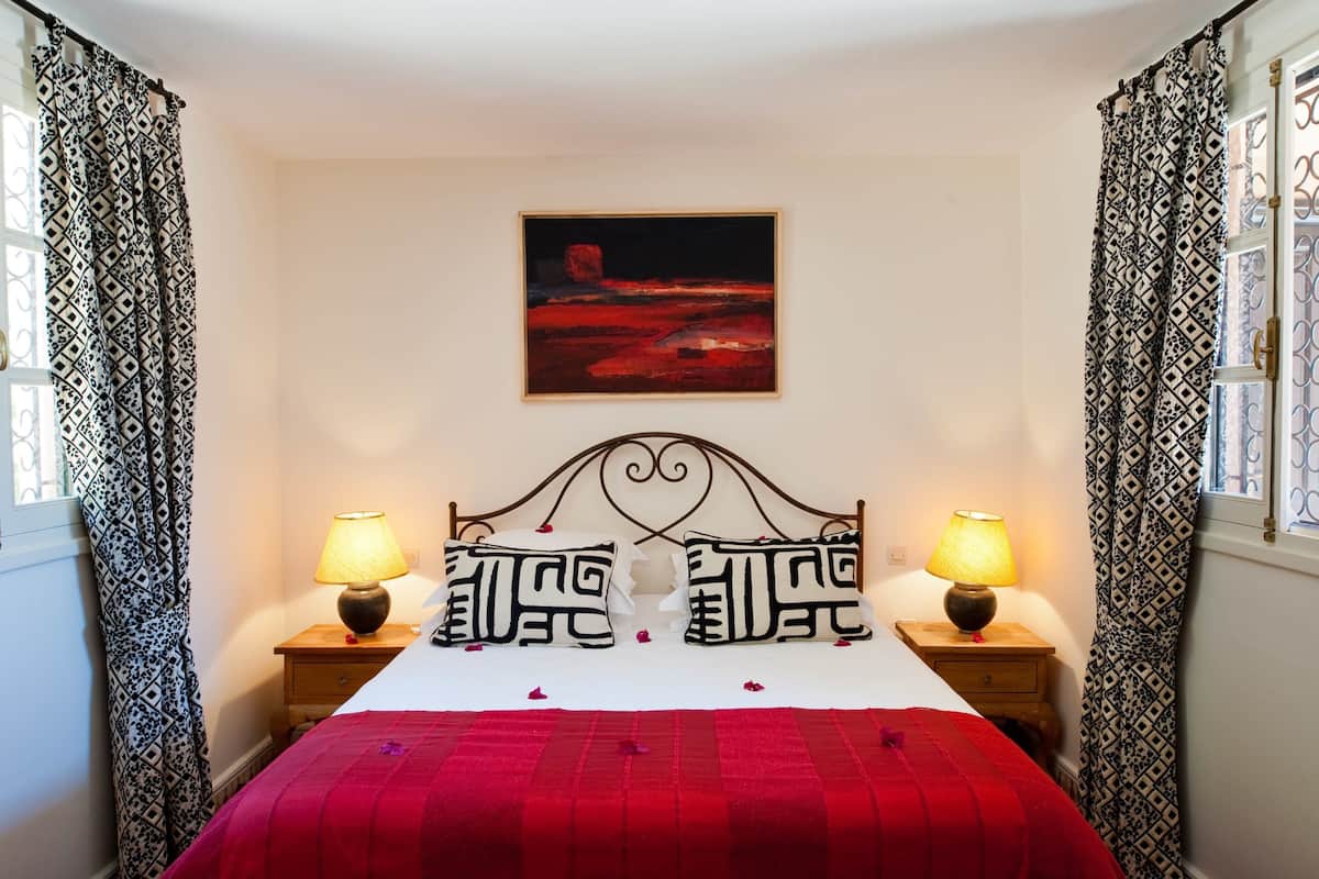 A bedroom with a bed, patterned curtains, a painting on the wall, and two bedside lamps.