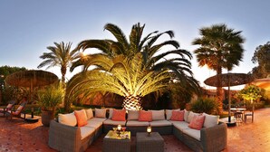 An outdoor seating area with a large sectional sofa, two side tables, and a round table with chairs. - Dar Maktoub (Inezgane)