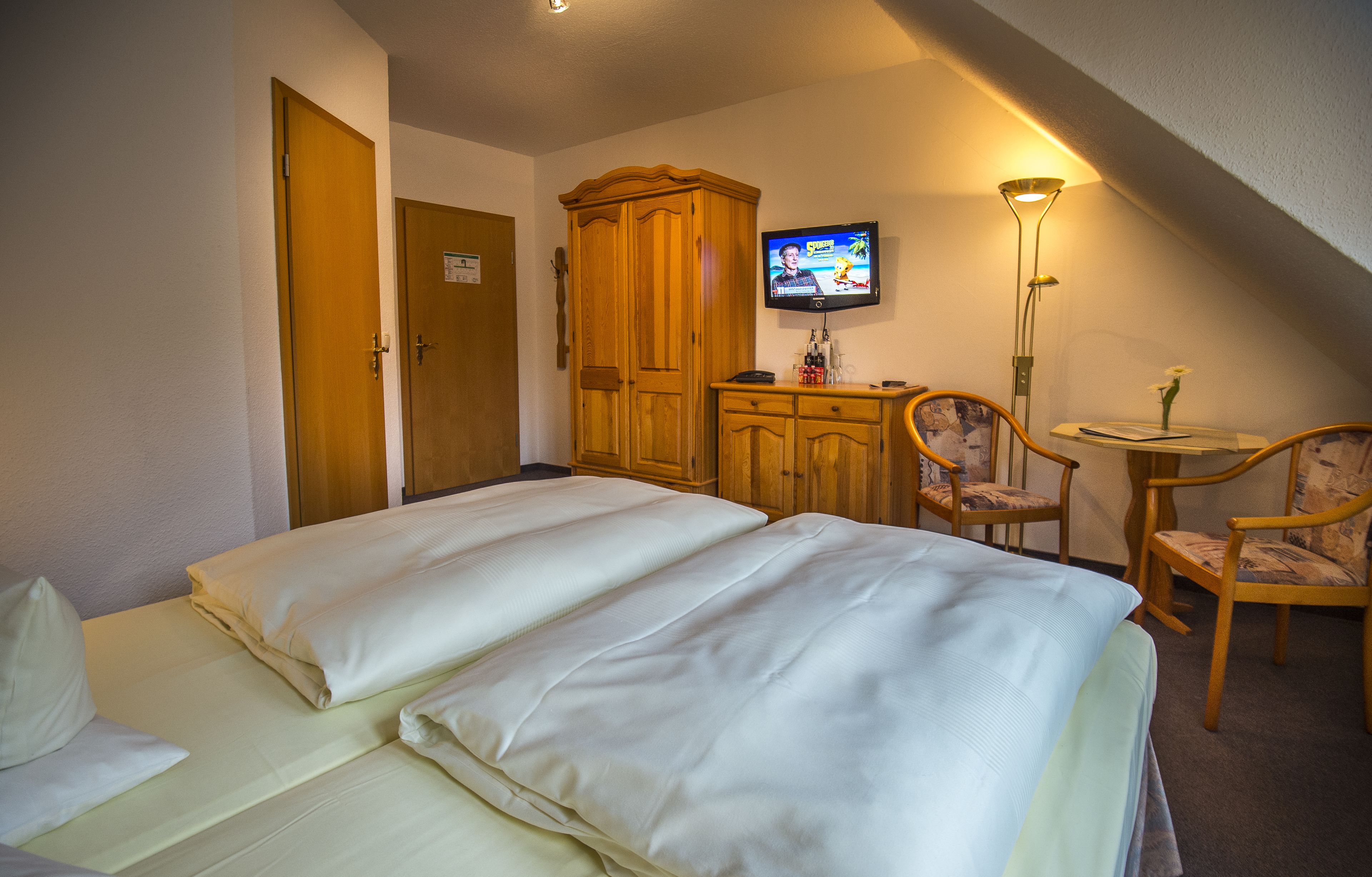 Habitación de hotel con dos camas, un armario de madera, un televisor, un escritorio con una silla y una lámpara.