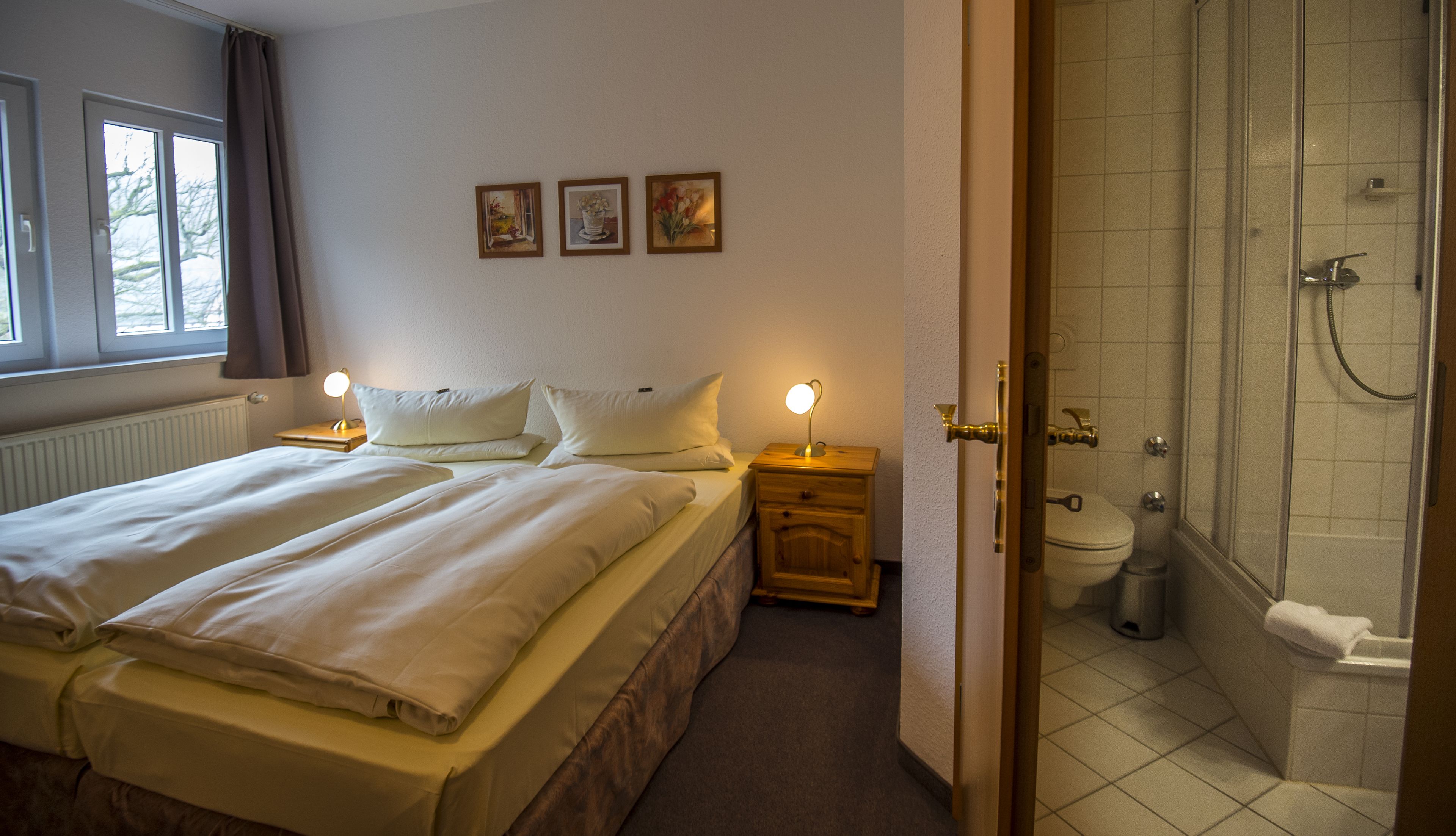 Une chambre d’hôtel avec un lit, des tables de chevet, une douche et trois tableaux encadrés au mur.