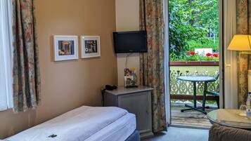 A hotel room with a single bed, a desk with a computer, a TV, and a balcony with a table and chair.