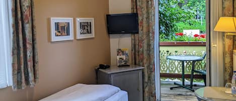 A hotel room with a single bed, a desk with a computer, a TV, and a balcony with a table and chair.