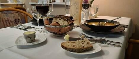 Una mesa con pan, sopa, copas de vino y una vela.