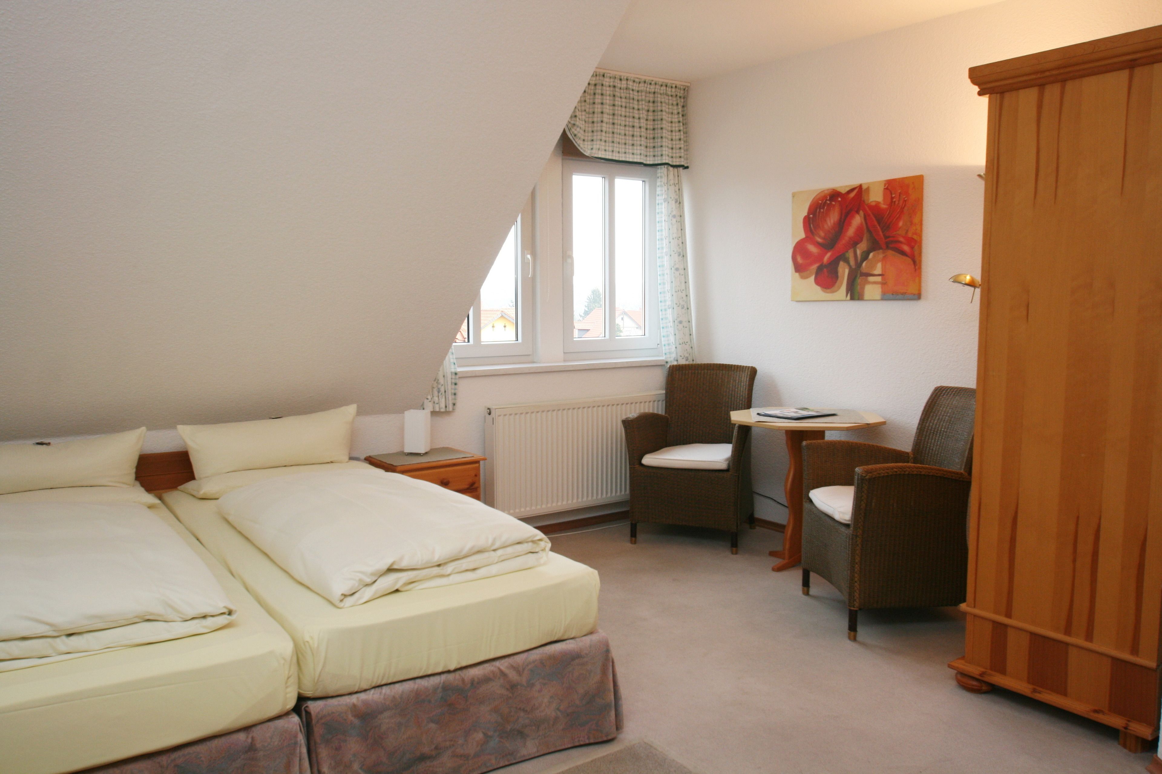 Een slaapkamer met twee bedden, een raam, een stoel, een tafel en een kledingkast.