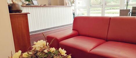 Un espace d’accueil avec un canapé rouge, un bureau en bois et un vase de fleurs.
