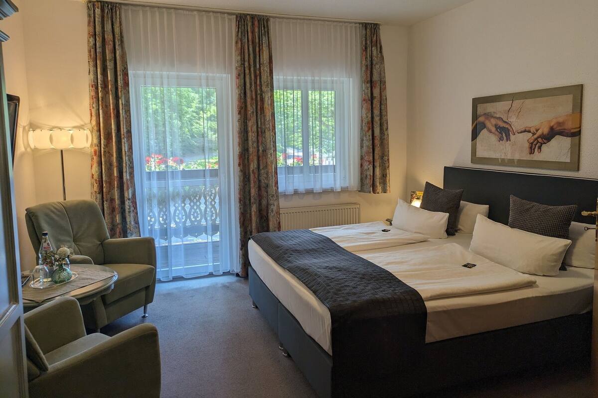 A hotel room with a bed, a chair, a small table, and a window with curtains.