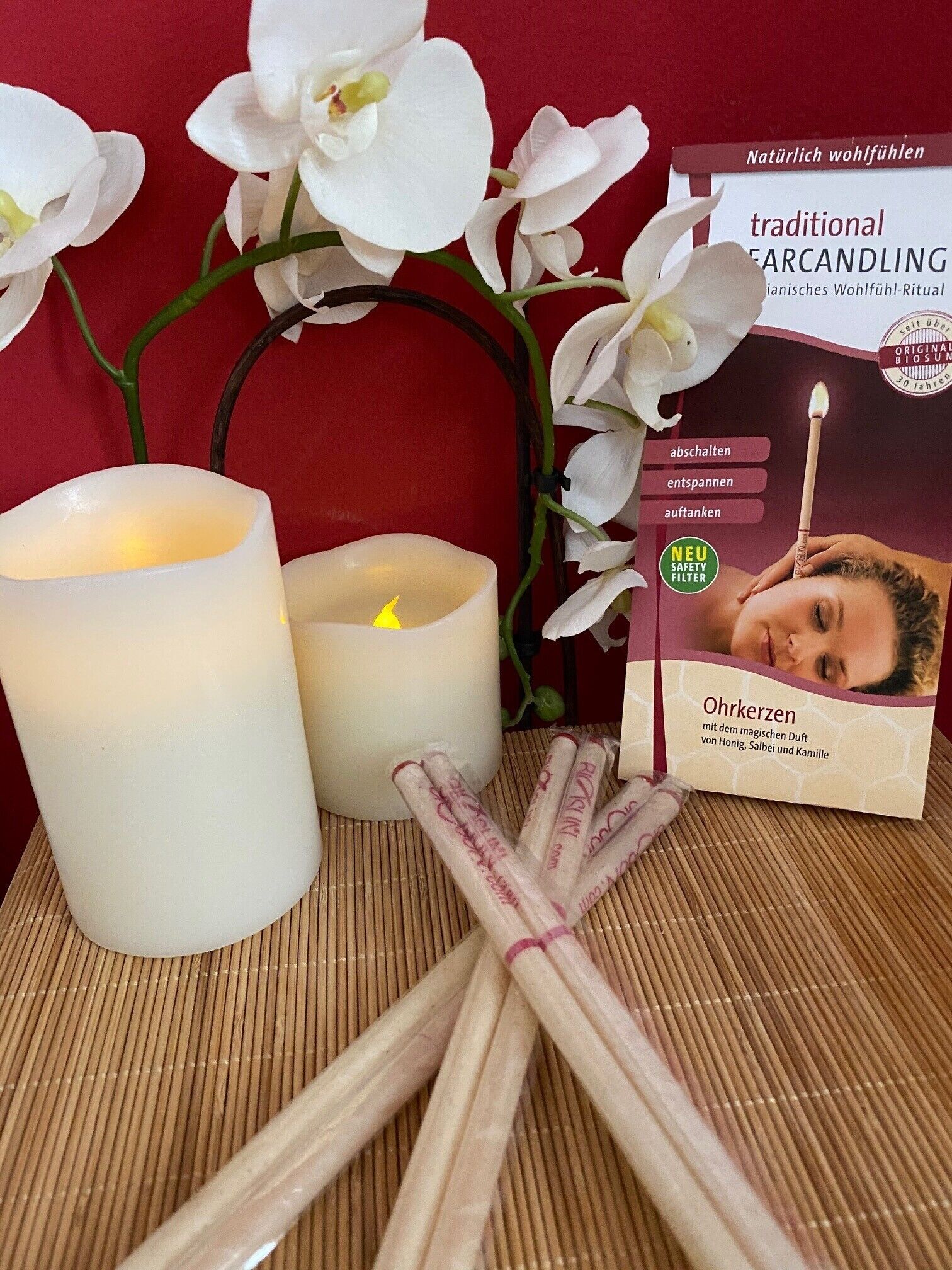 Una vela, una caja de palitos de incienso y orquídeas blancas sobre un tapete de bambú.