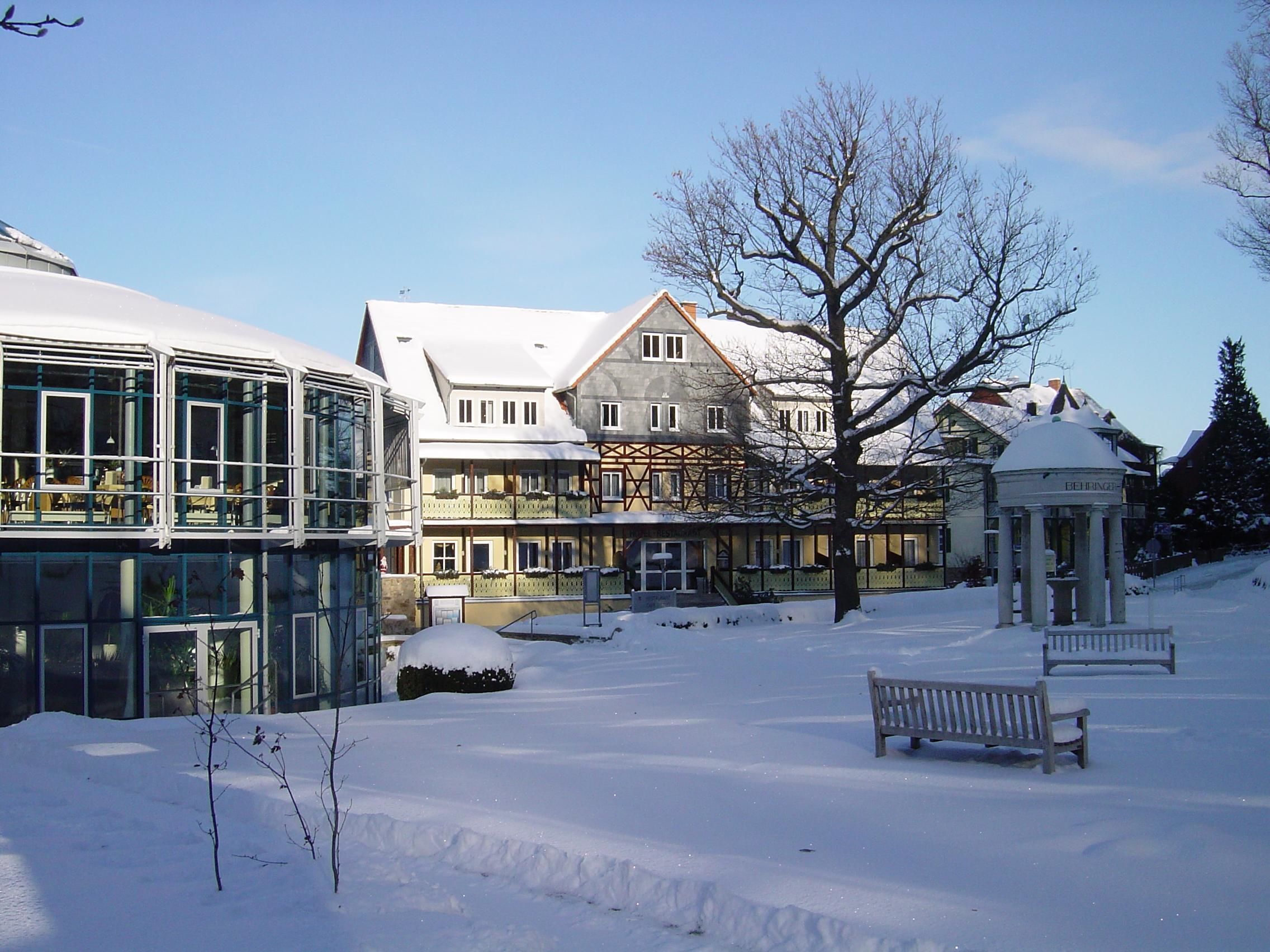 Een met sneeuw bedekte binnenplaats met een tuinhuisje, bankjes en een gebouw met veel ramen en balkons.