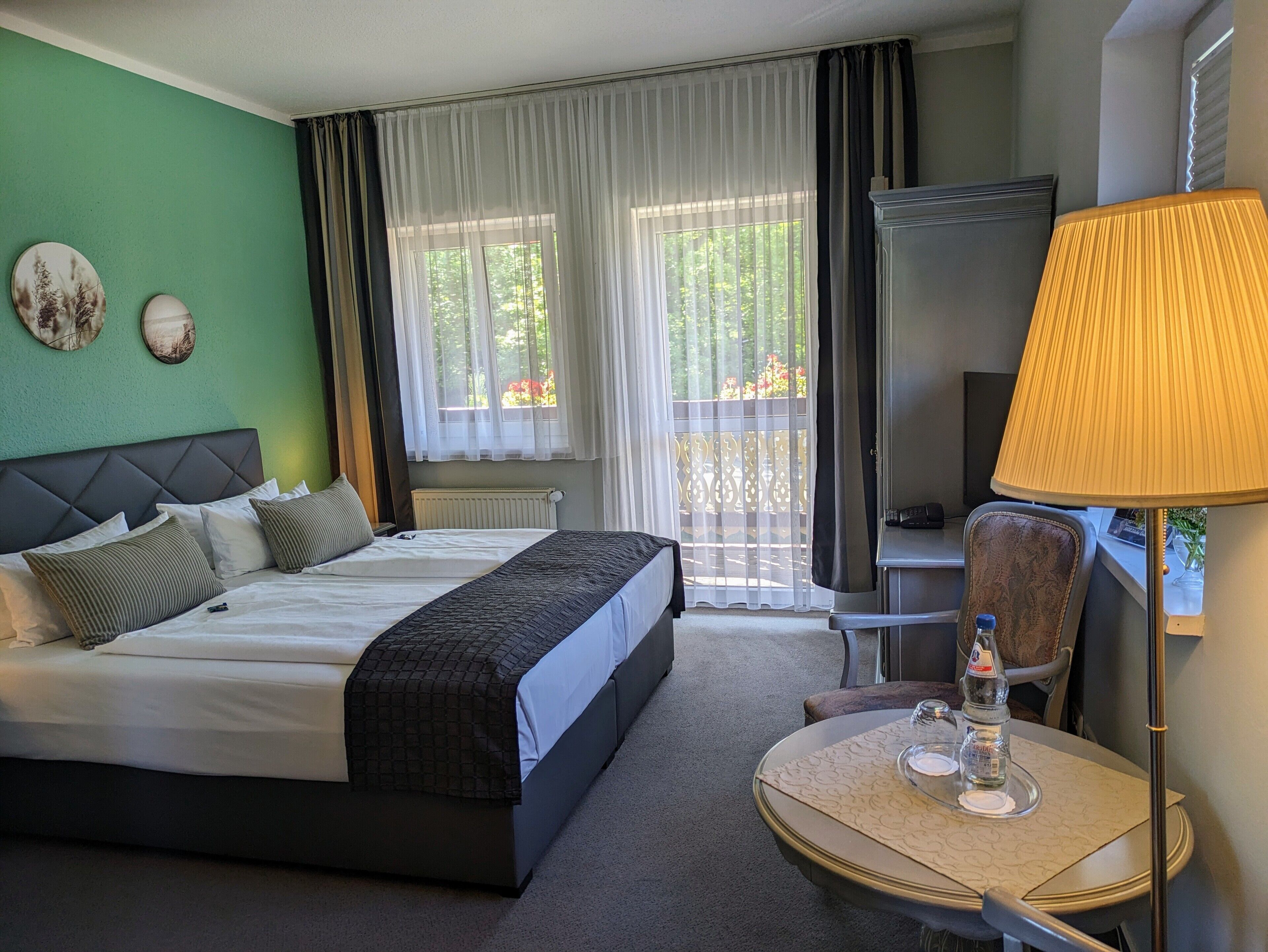 Une chambre d’hôtel avec un lit, un bureau doté d’une lampe, une chaise et une vue sur la verdure environnante.