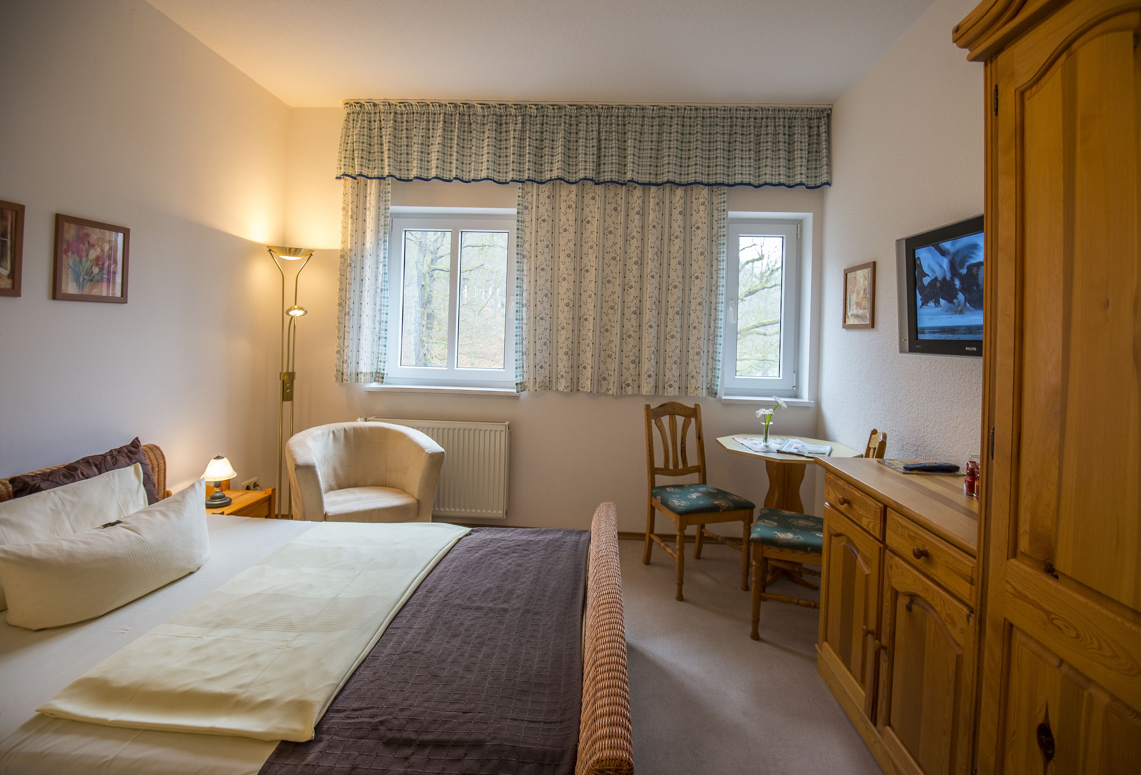 Una habitación de hotel con cama, escritorio, silla, lámpara, televisor y armario.