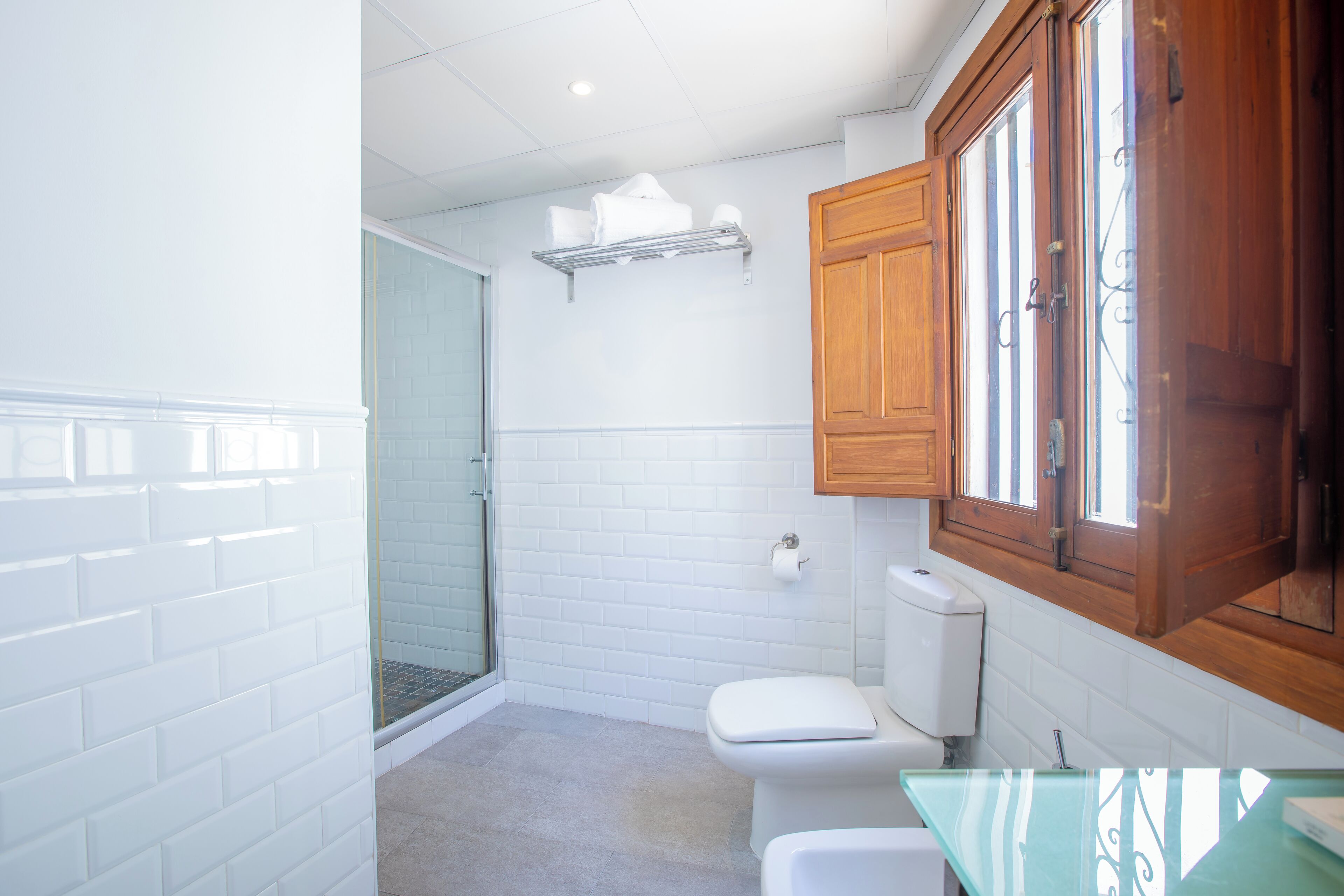 A bathroom with white subway tiles, a glass shower enclosure, a white toilet, and wooden cabinets.