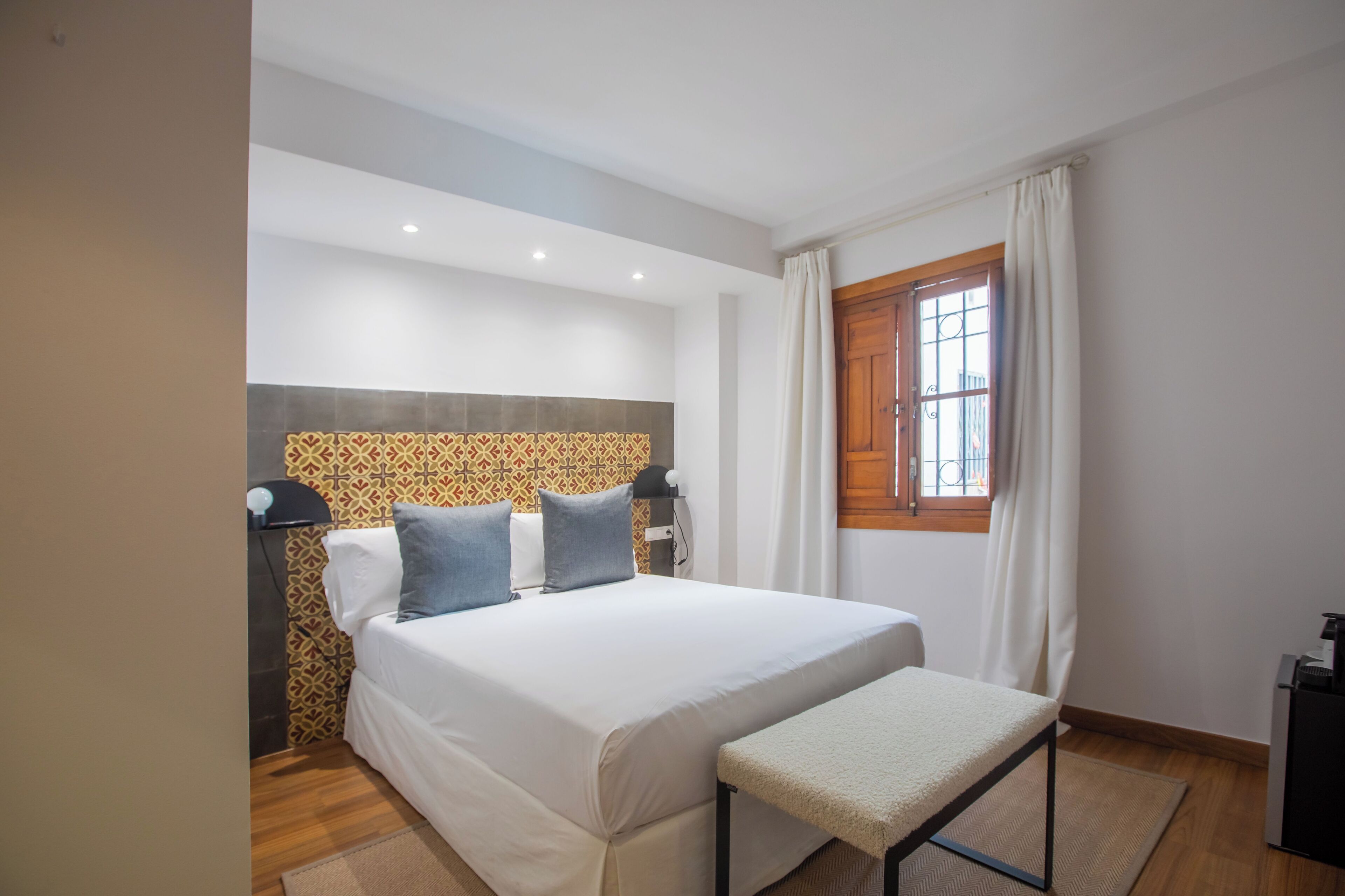 Un dormitorio con cama, mesita de noche y ventana con cortinas.