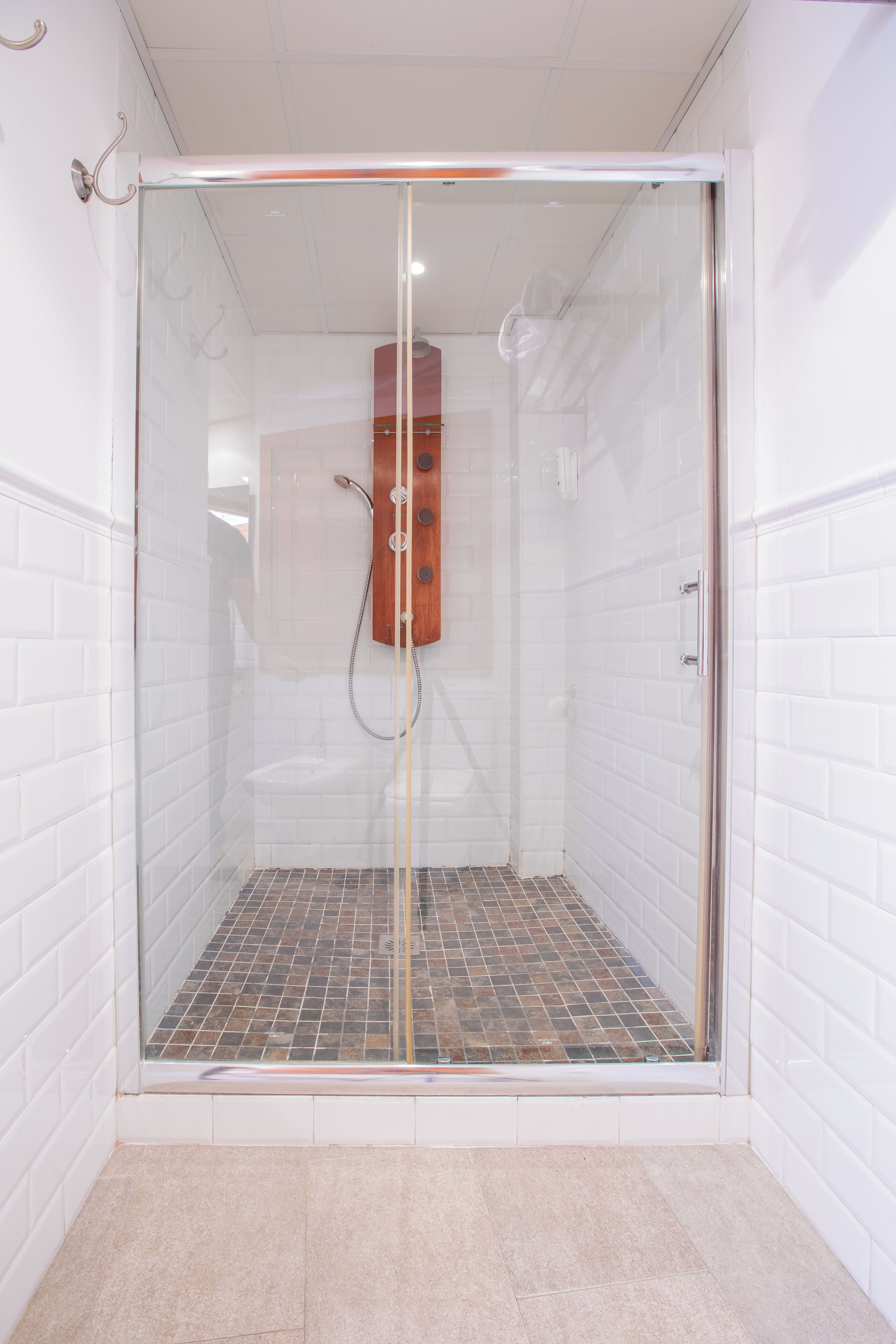 A glass-enclosed shower stall with a tiled floor and a wooden panel on the wall.