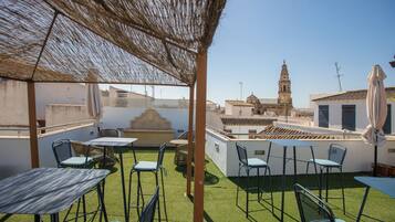 Un patio al aire libre con mesas y sillas, una pérgola y vistas a una torre histórica.
