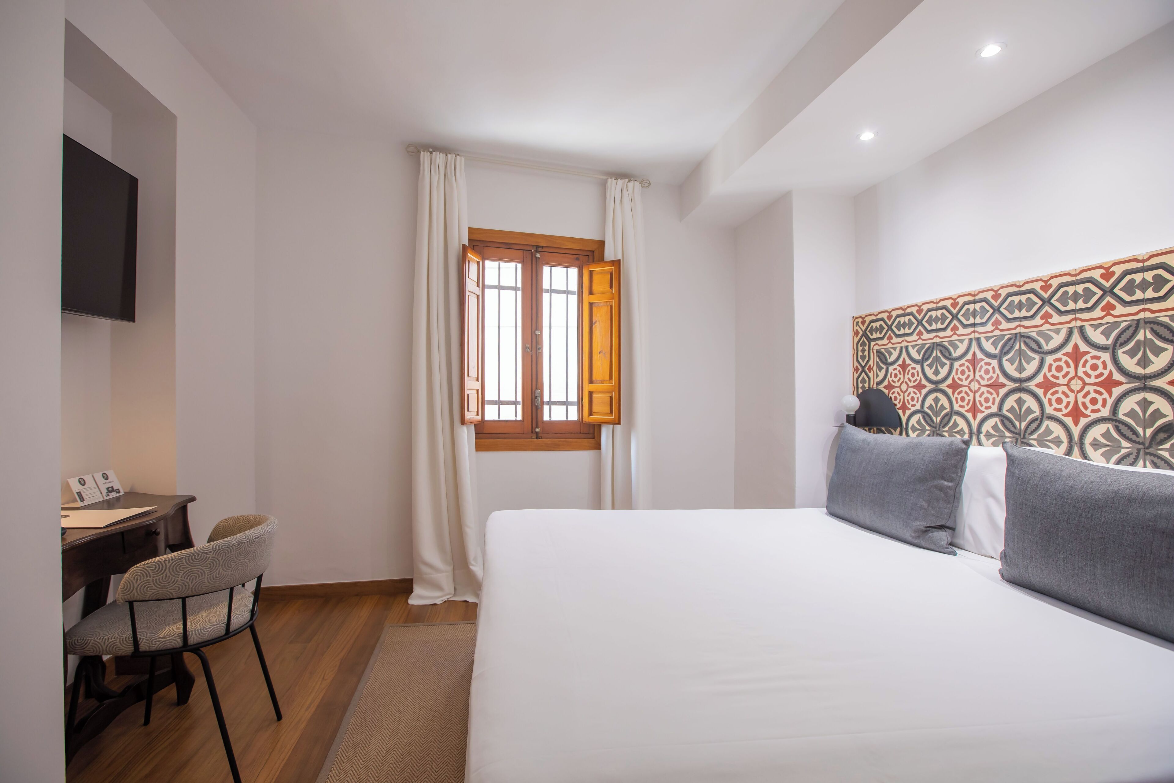 Une chambre d’hôtel comprenant un lit, un bureau avec une chaise, un téléviseur fixé au mur et une fenêtre avec des rideaux.