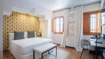 Un dormitorio con cama, banco, escritorio, silla y papel tapiz estampado.