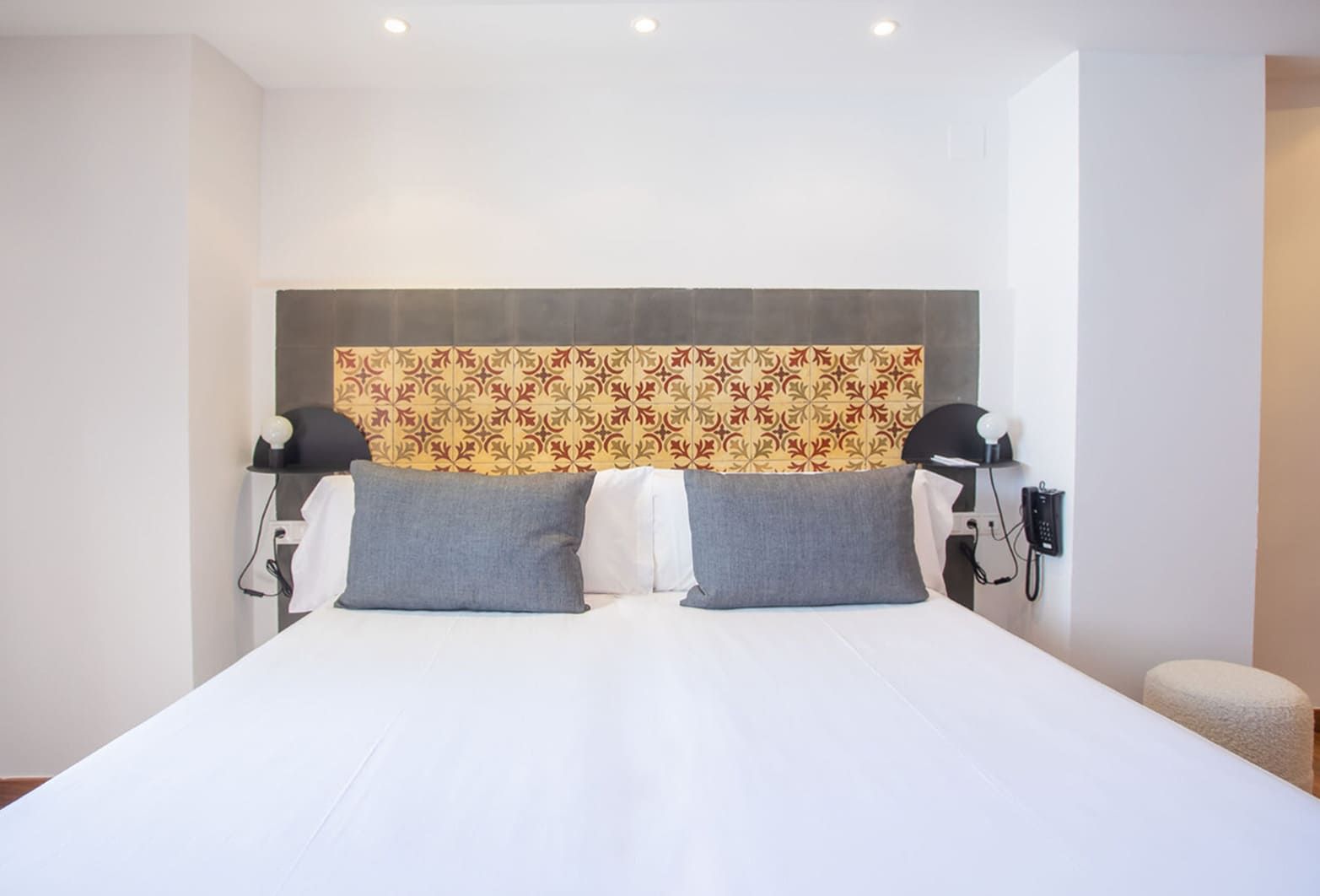 Ein Hotelzimmer mit einem großen Bett, zwei Nachttischlampen, einem gemusterten Kopfteil und einem Telefon an der Wand.