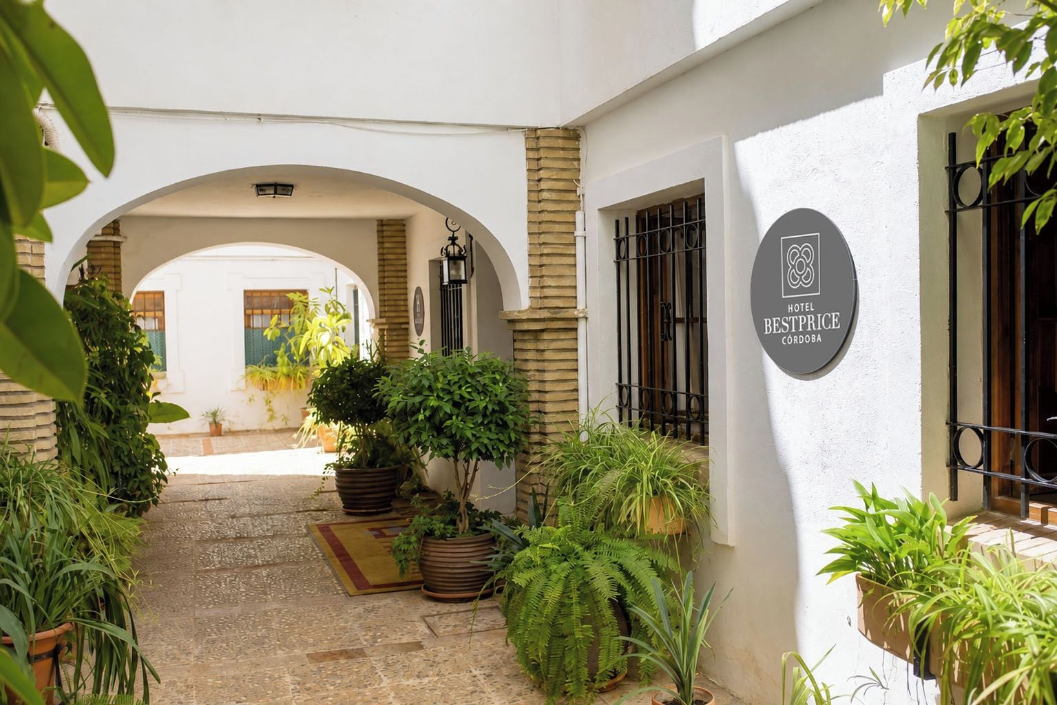 Un patio con un edificio blanco, plantas en macetas y un letrero que dice Hotel Bestprice Córdoba.