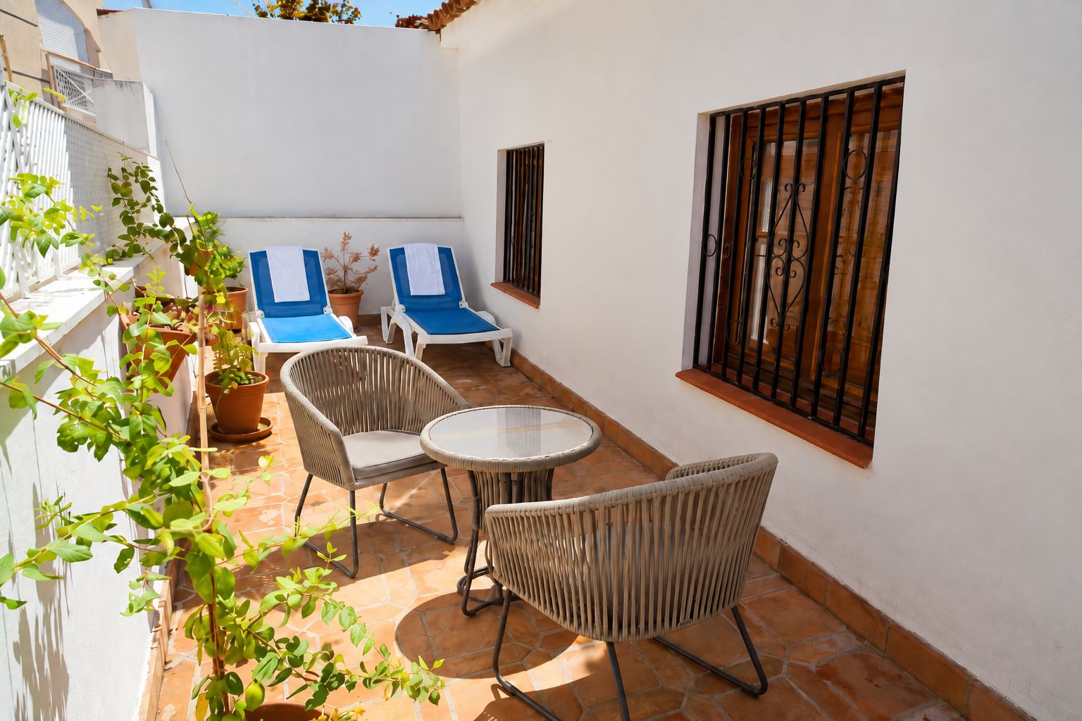 A patio with wicker furniture, a small table, and two blue lounge chairs.
