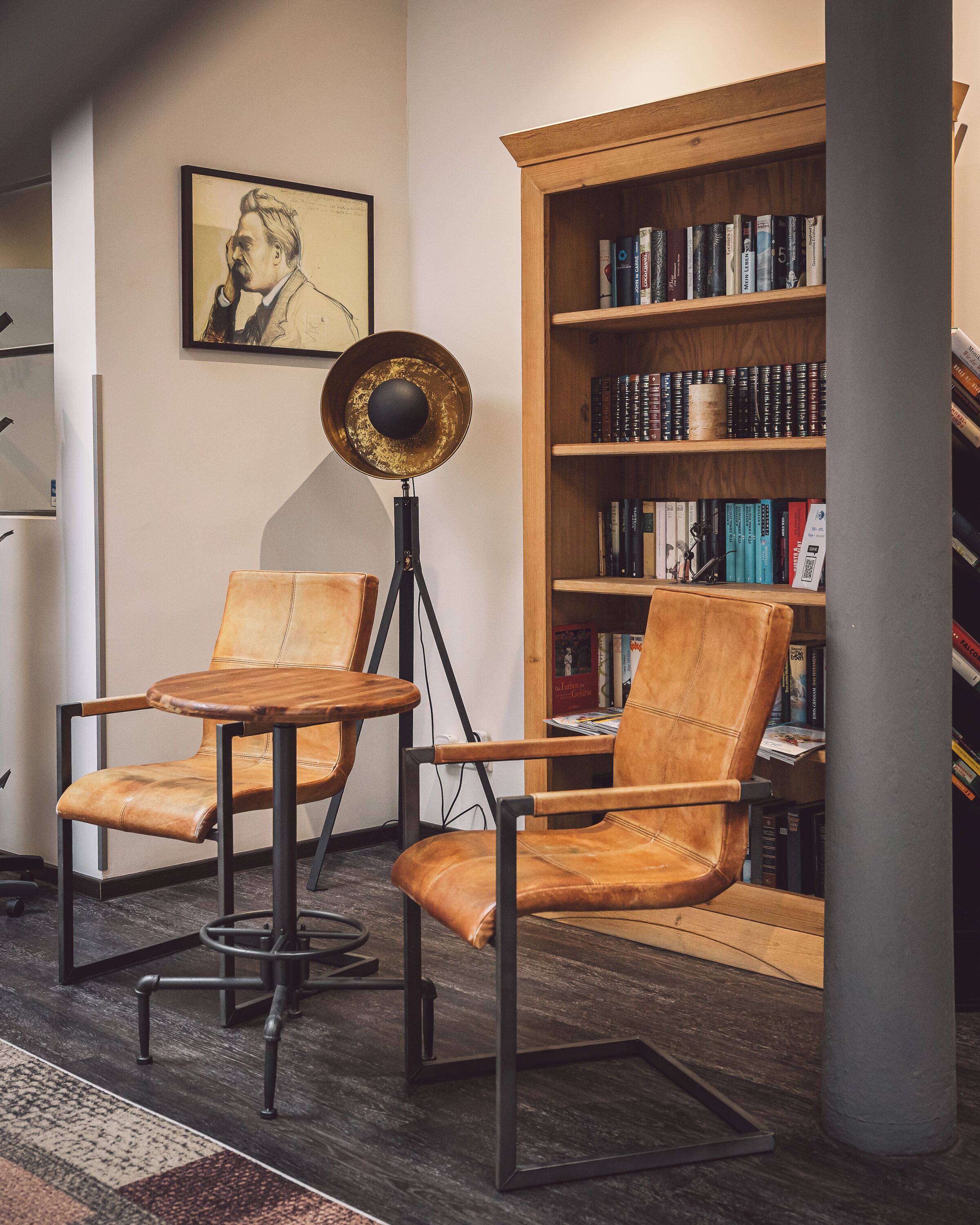 Un rincón de lectura con dos sillones de cuero, una lámpara de pie y una estantería llena de libros.