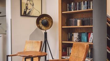 Un rincón de lectura con dos sillones de cuero, una lámpara de pie y una estantería llena de libros.