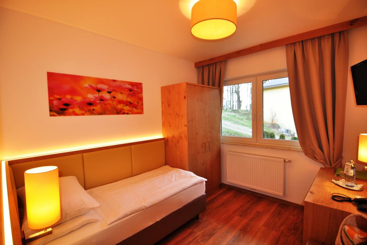 A bedroom with a bed, a wooden wardrobe, a window with curtains, and a painting on the wall.