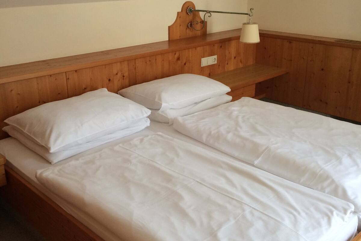 A wooden bunk bed with white bedding in a room with a sloped ceiling and a wooden headboard.